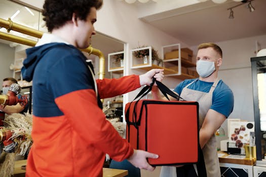 pexels-photo-4393668-4393668 Two men exchanging a food delivery bag indoors, both wearing face masks.